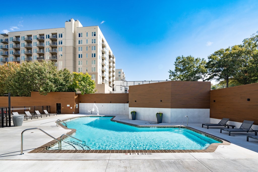 A large swimming pool with lounge chairs and a fence around it.