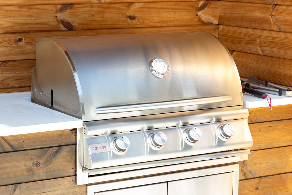 A silver gas grill with four burners and a side burner is mounted on a wooden wall.