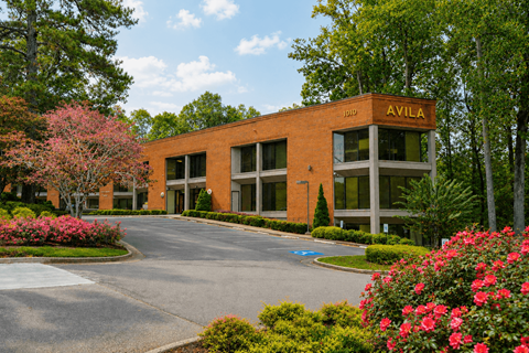A building with the word "AVILA" on it is surrounded by trees and flowers.