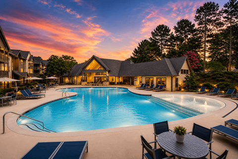A large outdoor swimming pool surrounded by lounge chairs and a table with a potted plant.