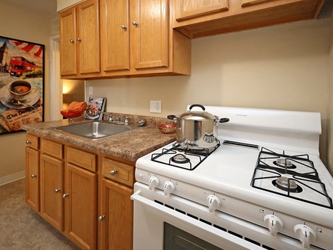 A white gas stove with four burners is in the middle of a kitchen with wooden cabinets.