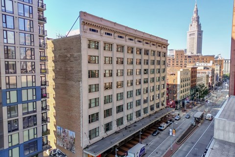 A city street with a large building in the middle and a tall building in the background.