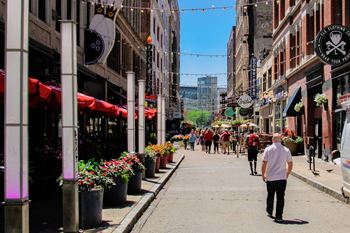 A man walking down a street lined with flower pots and storefronts.