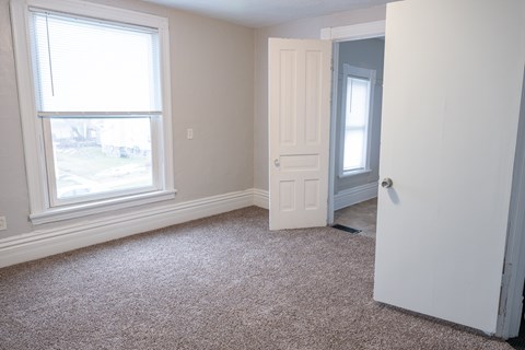 A room with a carpeted floor, a window, and a door.