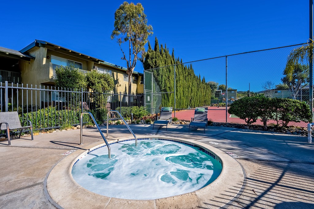A hot tub sits in the middle of a patio surrounded by a fence. A hot tub sits in the middle of a patio surrounded by a fence.