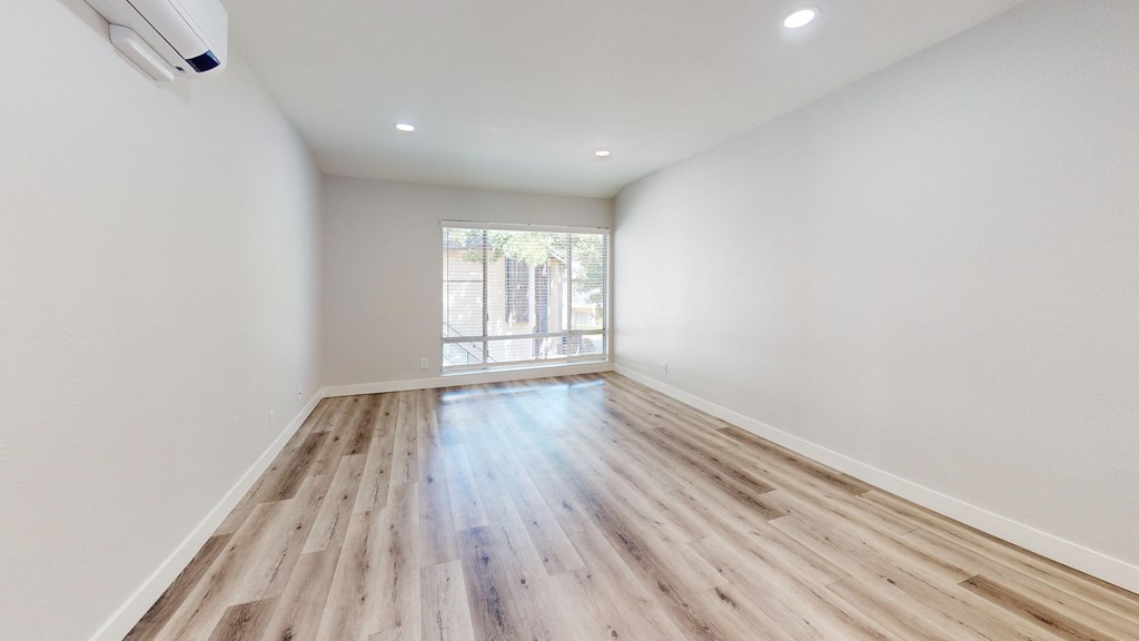 a living room with white walls and wood flooring and a window
