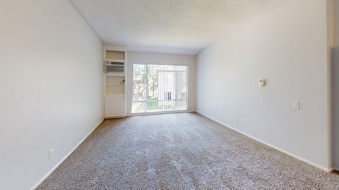 a spacious living room with carpet and a door to a balcony