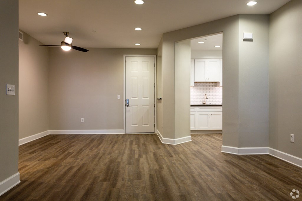 an empty living room with a kitchen in the background
