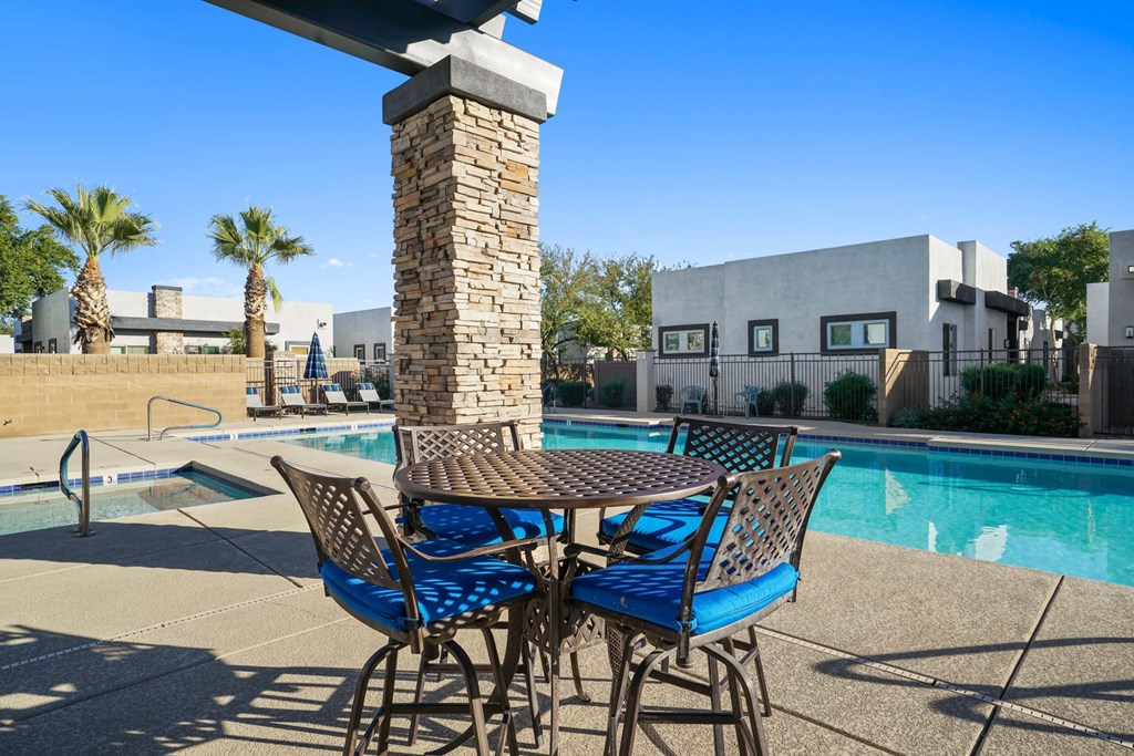 A table with chairs is in the foreground of a pool area.
