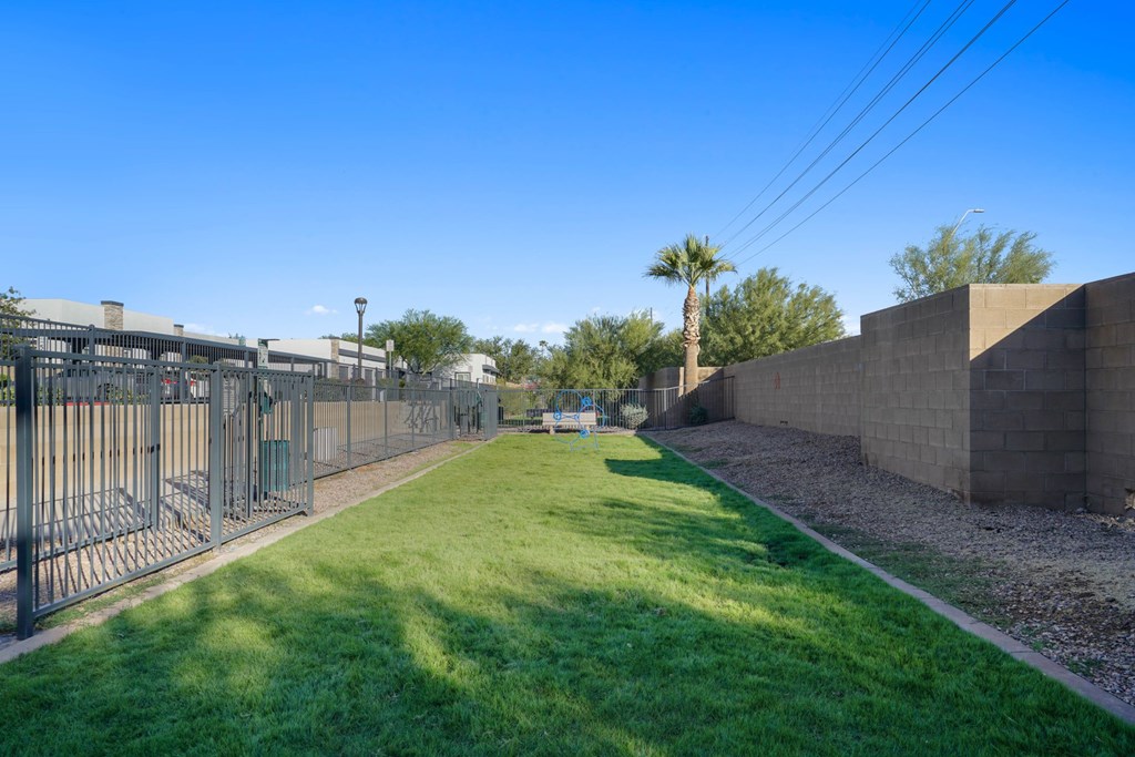 A long grassy area with a fence on the left and a wall on the right.