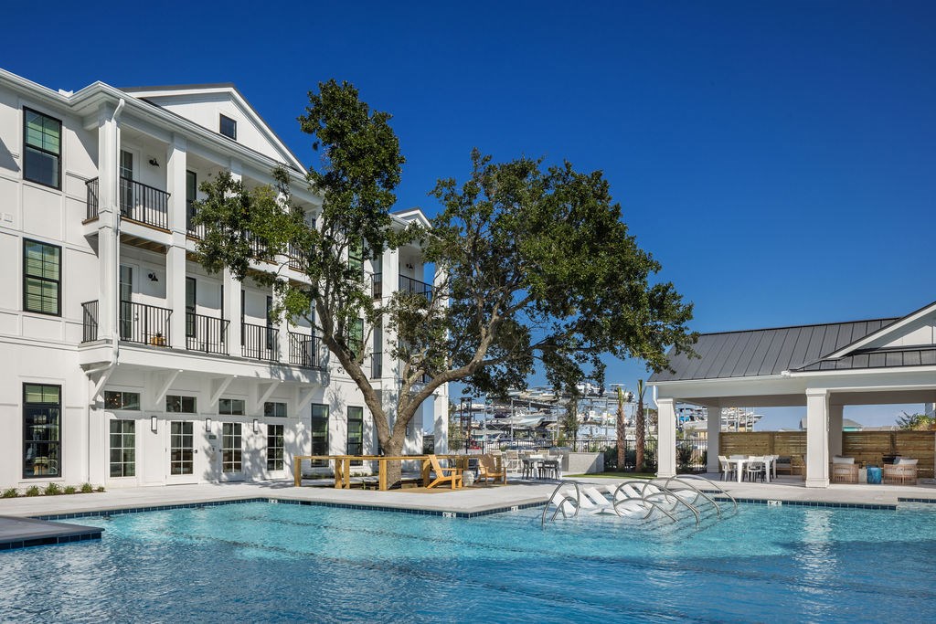 A large swimming pool is surrounded by a white building with balconies.