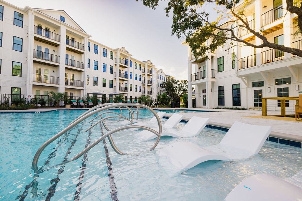 A swimming pool with white lounge chairs in front of apartment buildings.