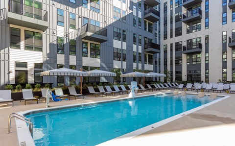 A swimming pool with lounge chairs and umbrellas in front of a modern building.