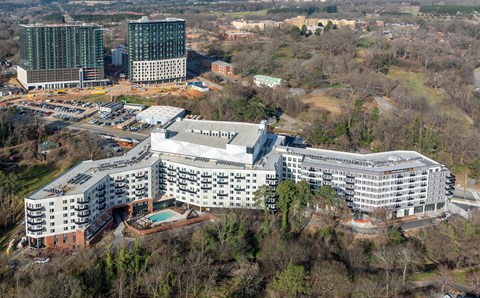 A large white building with a pool in the courtyard is surrounded by trees.