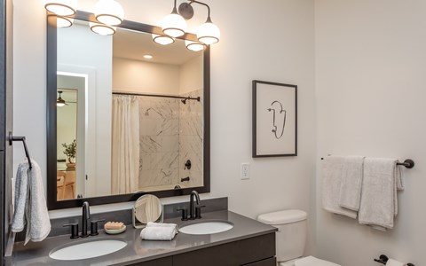 A bathroom with a large mirror, two sinks, and a toilet.