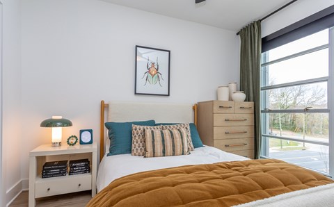 A bedroom with a bed, nightstand, and a painting of a mosquito on the wall.