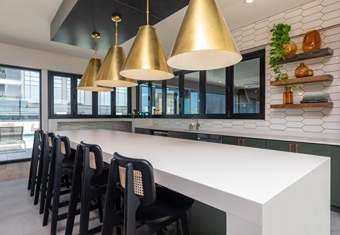 a long white counter in a kitchen with black chairs and brass lights