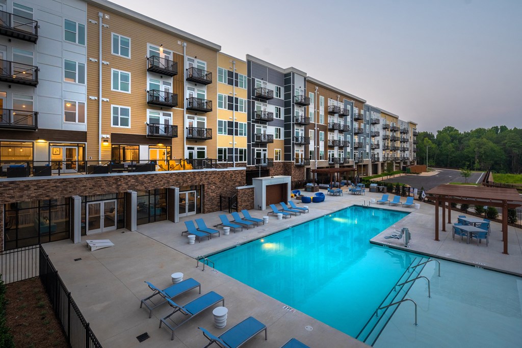 an outdoor swimming pool with chaise lounge chairs and a fire pit in front of an apartment