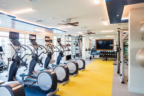 A gym with a row of stationary bikes and a television.