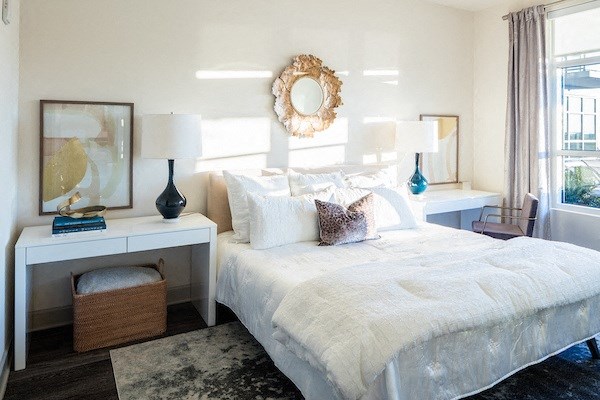 A bedroom with a large bed, a mirror, and a window with curtains.