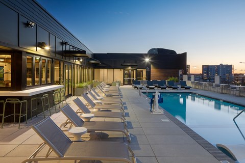 a pool area with lounge chairs and a bar with a city skyline in the background