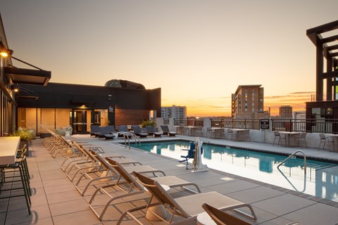 a rooftop pool with lounge chairs and a city skyline in the background
