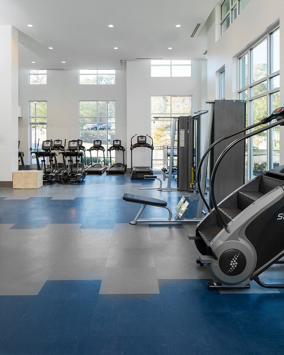 a gym with cardio equipment and chairs in a building with large windows