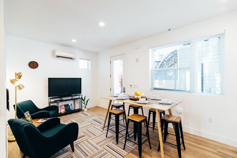 A living room with a black chair, a black sofa, a wooden table with four chairs and a television.