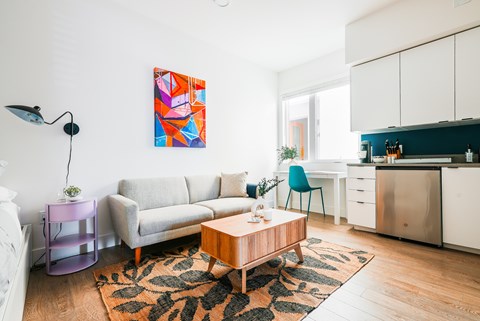 A living room with a grey couch, a wooden coffee table, and a painting on the wall.