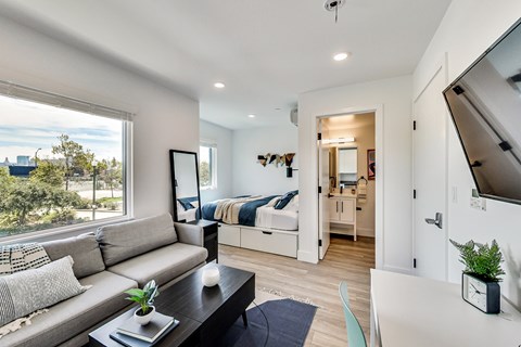 A modern living room with a grey couch and a large window overlooking a cityscape.