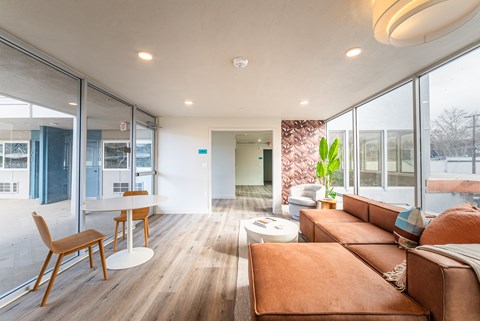 A modern living room with a brown leather couch and wooden chairs.