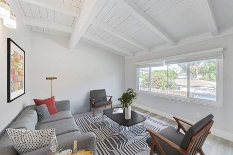 A living room with a grey couch, a black chair, a small table, and a painting on the wall.