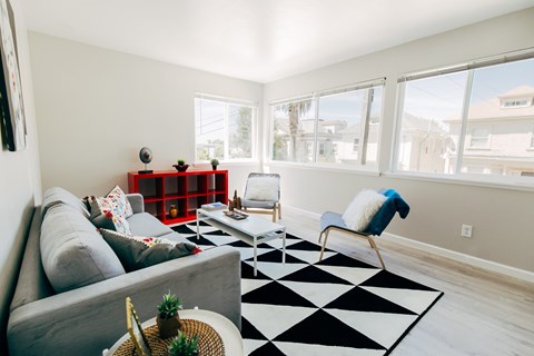 A living room with a grey couch, a black and white rug, and a window with a view of the outside.