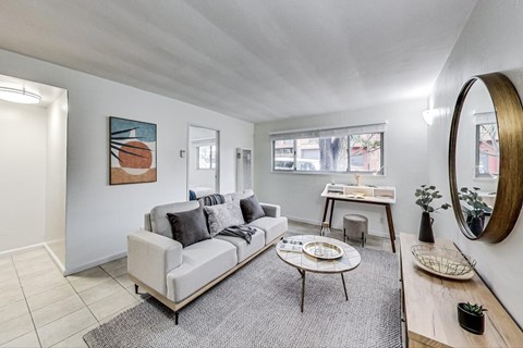 A living room with a grey couch, a round mirror, and a painting on the wall.