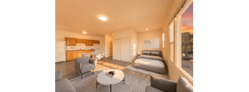 A well-lit bedroom with a large bed and a kitchen area with a refrigerator.