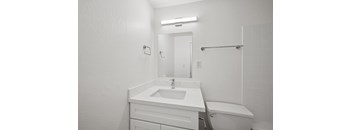 A white bathroom with a sink, mirror, and toilet.
