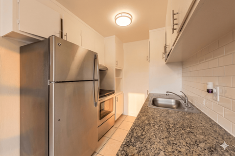 A kitchen with a granite counter top and a stainless steel refrigerator.