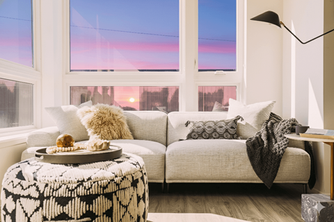 A cozy living room with a couch, a table with a tray of food, and a window with a view of the city.