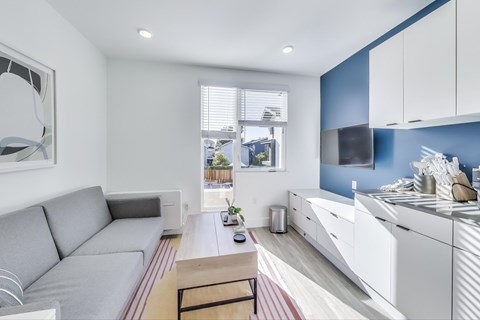 A modern living room with a grey sofa and a kitchen area with white cabinets.
