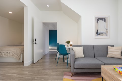 A living room with a grey couch, a blue chair, and a painting on the wall.