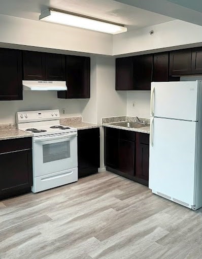 A white refrigerator stands in a kitchen with dark brown cabinets.