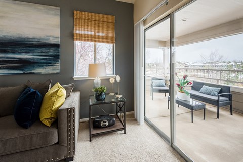 A living room with a grey couch, a table with a lamp and a painting on the wall.