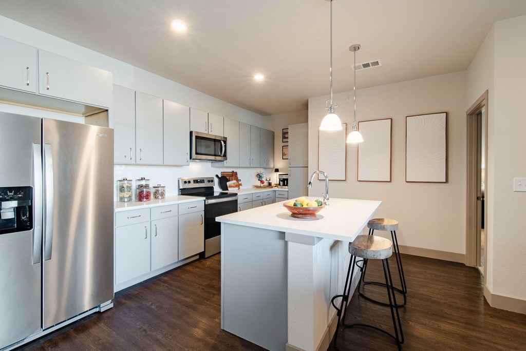 a kitchen with white cabinets and a white island with two stools at Parkside at Littleton Village, Littleton, CO