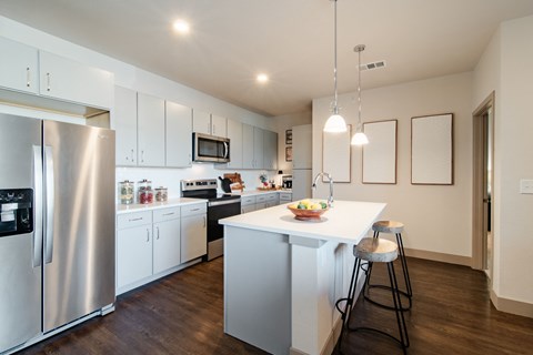 a kitchen with white cabinets and a white island with two stools at Parkside at Littleton Village, Littleton, CO