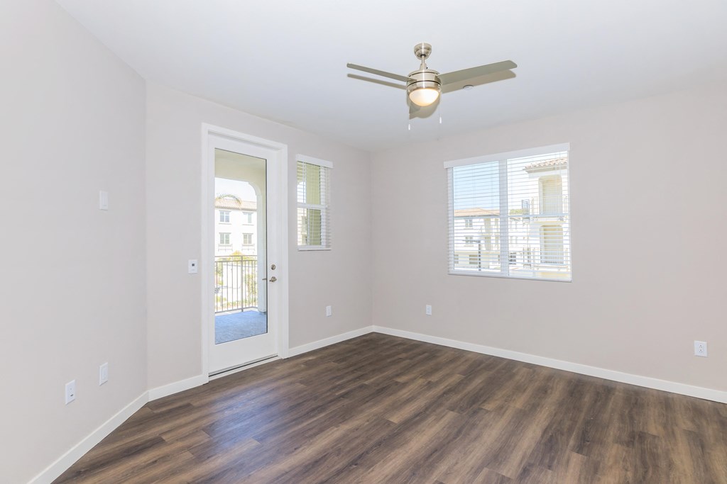 an empty living room with a ceiling fan and a door to a balcony