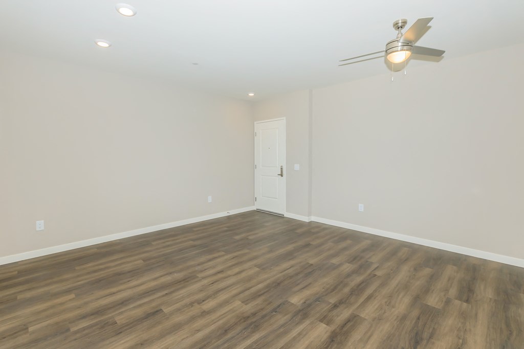 a living room with white walls and wood floors and a ceiling fan