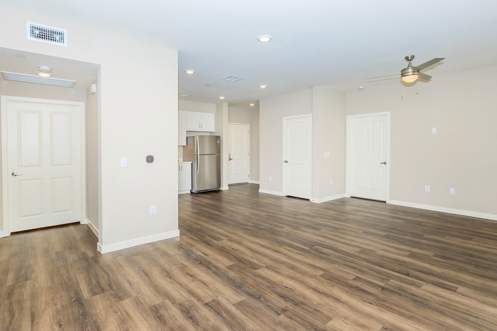 an empty living room with wood flooring and a kitchen