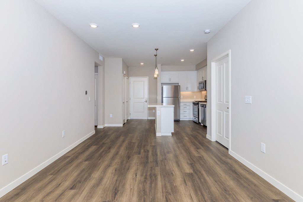a living room and kitchen with white walls and wood flooring