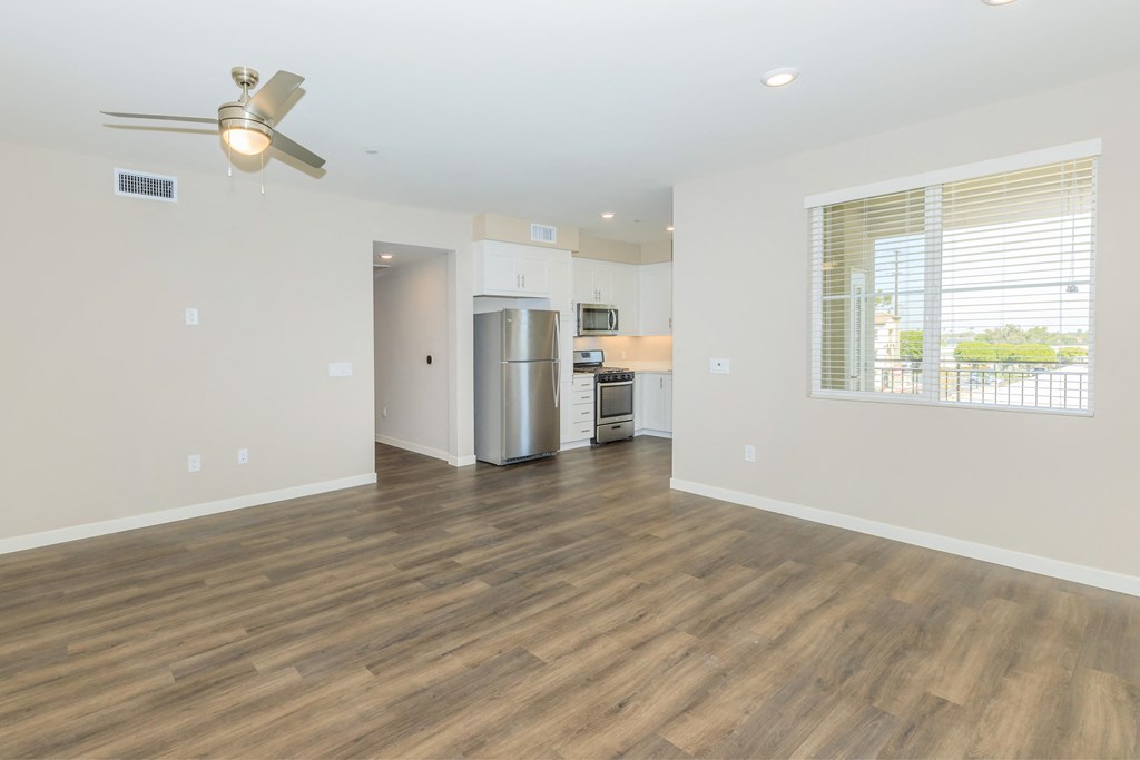 an empty living room with a large window and a kitchen