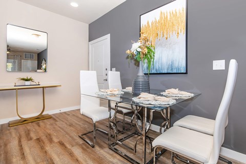 A dining room with a glass table and white chairs.